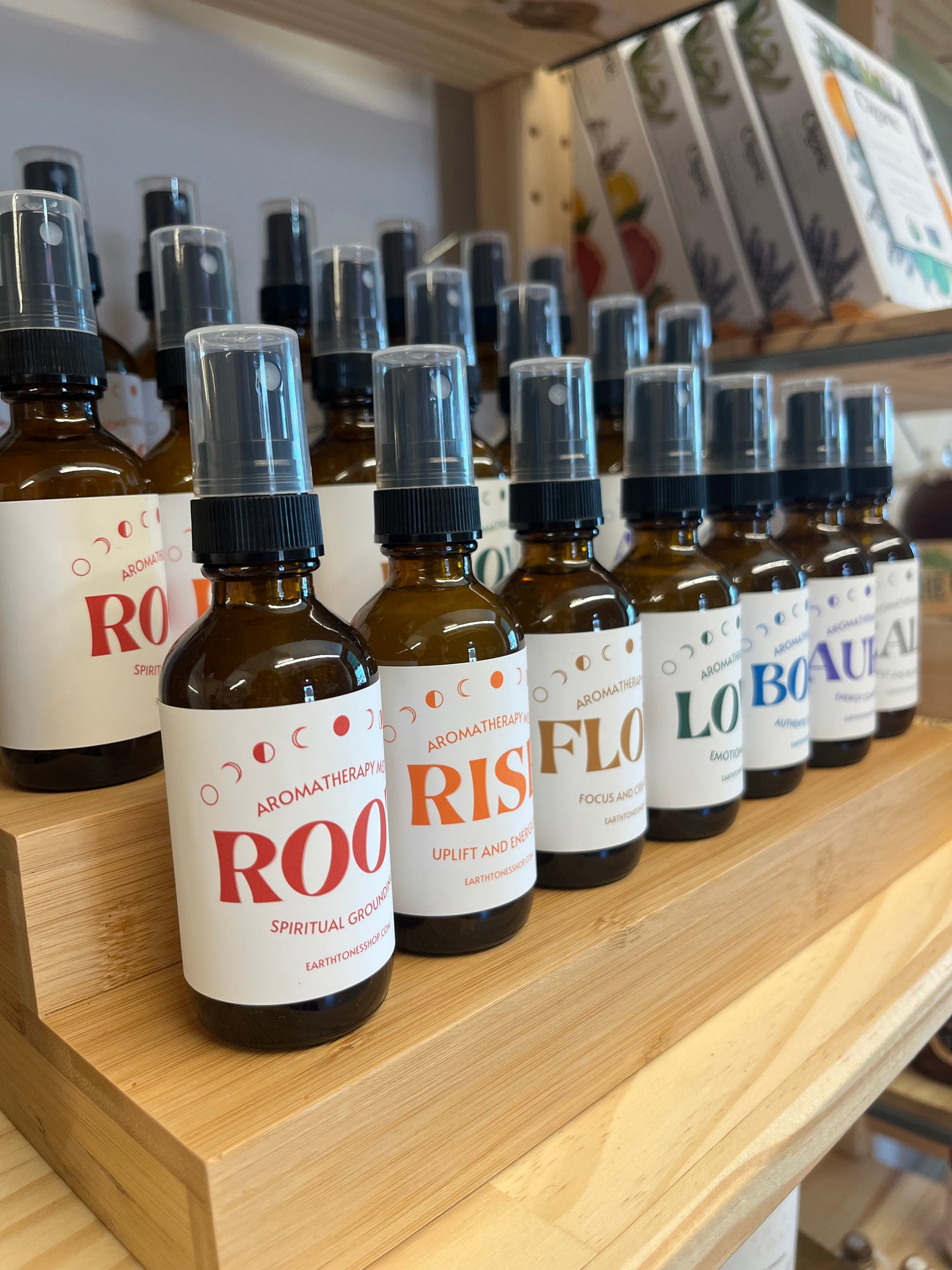 Row of Earthtones Aromatherapy Mists with white labels on a wooden shelf.