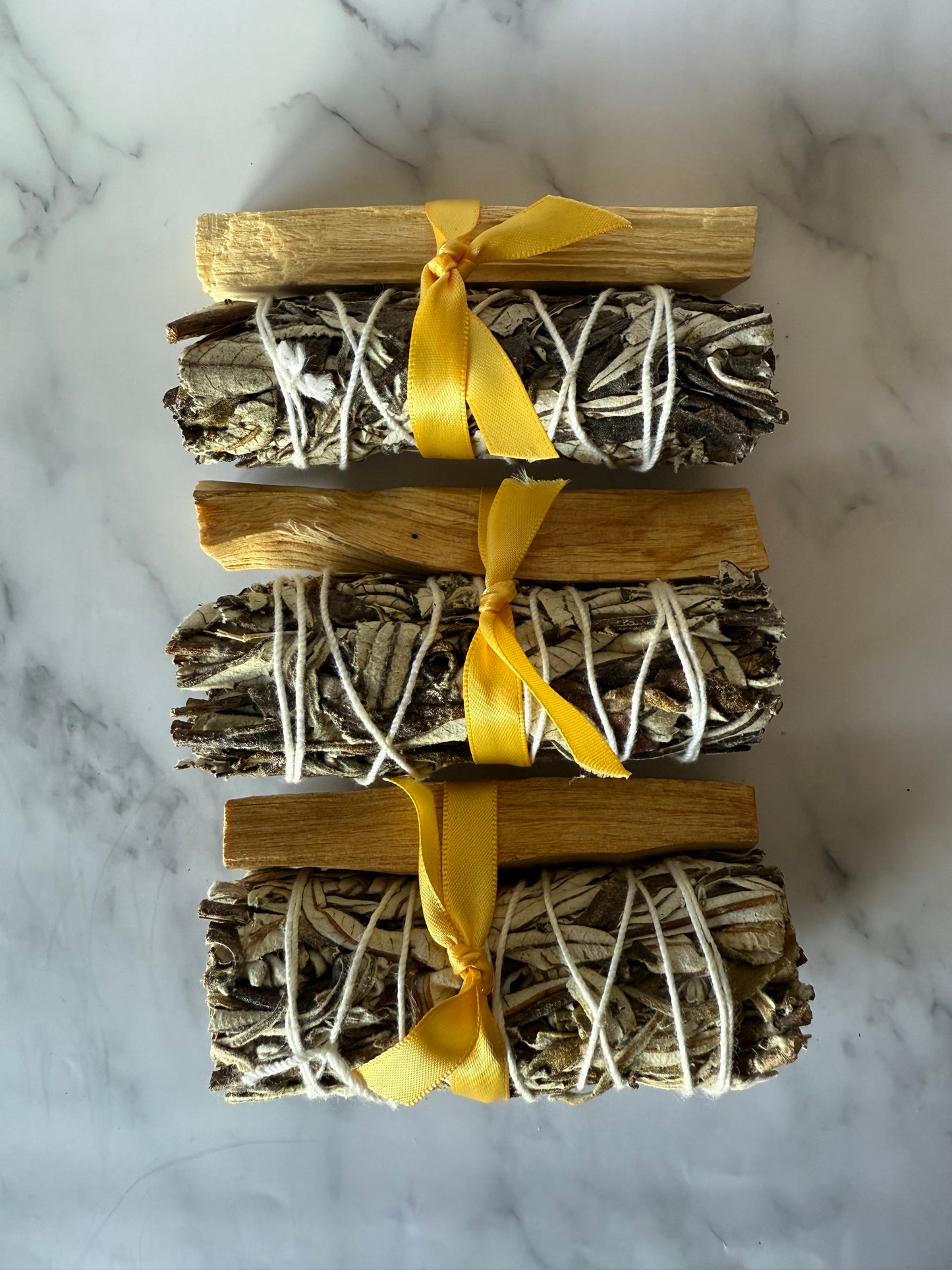 Three bundles of palo and yerba wrapped with yellow ribbons on a marble surface