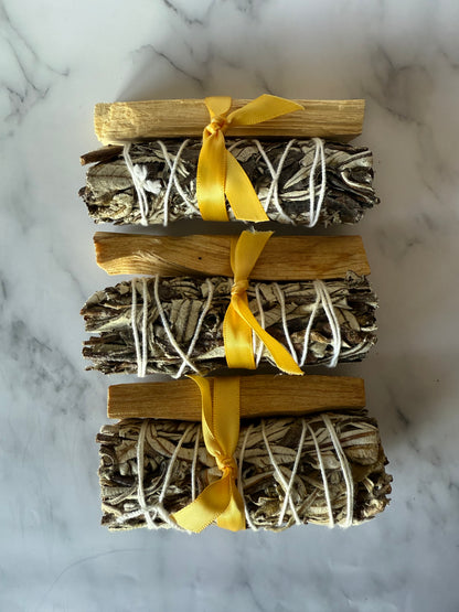 Three bundles of palo and yerba wrapped with yellow ribbons on a marble surface