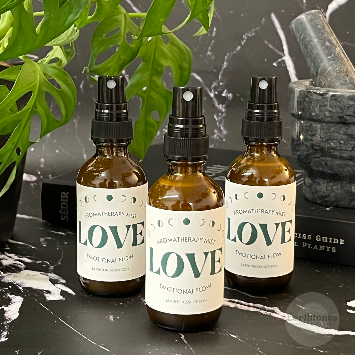 Three bottles of 'LOVE' aromatherapy mist on a dark surface with plants in the background.