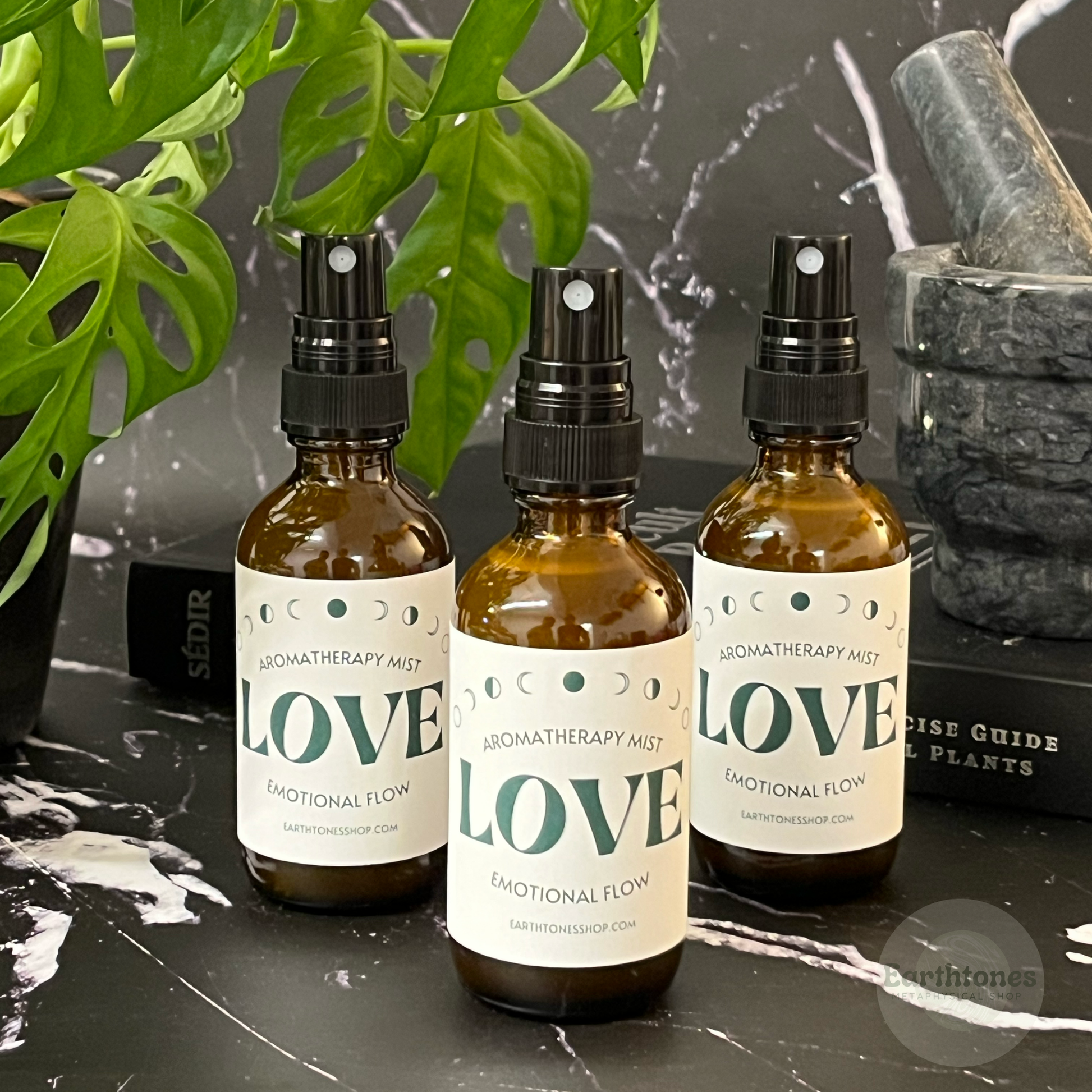 Three bottles of 'LOVE' aromatherapy mist on a dark surface with plants in the background.