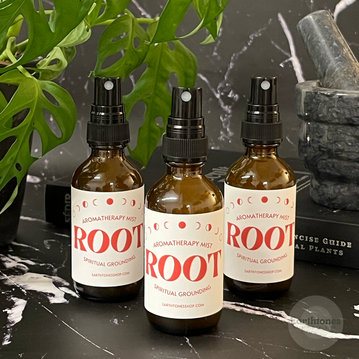 Three bottles of 'ROOT' aromatherapy mist on a dark surface with green leaves in the background.